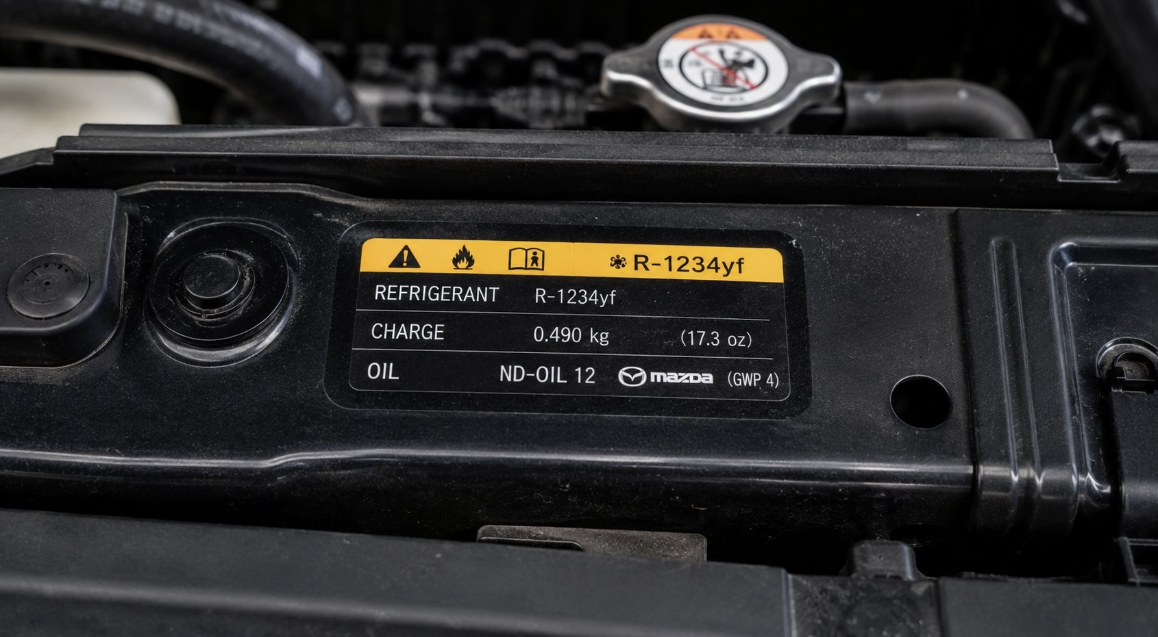 Underhood refrigerant label on a Mazda showing refrigerant type and charge amount