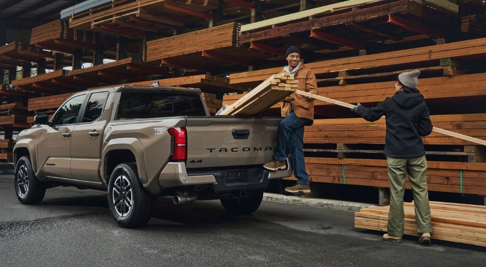 A couple loading the bed of a tan 2026 Toyota Tacoma TRD Sport.