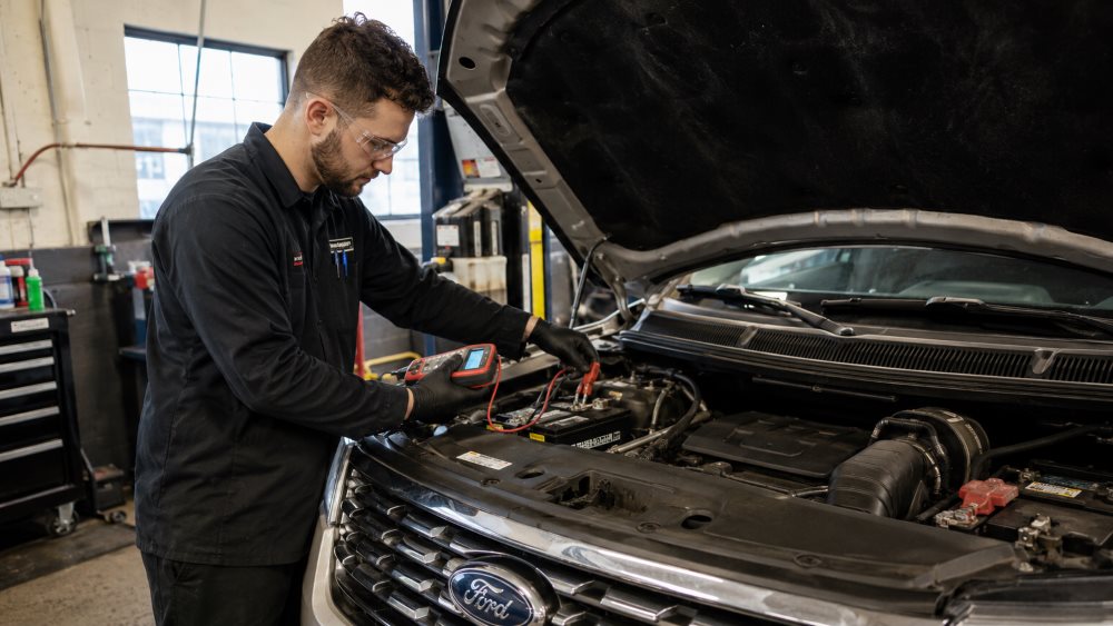 Technician testing a Ford vehicle battery in a service bay