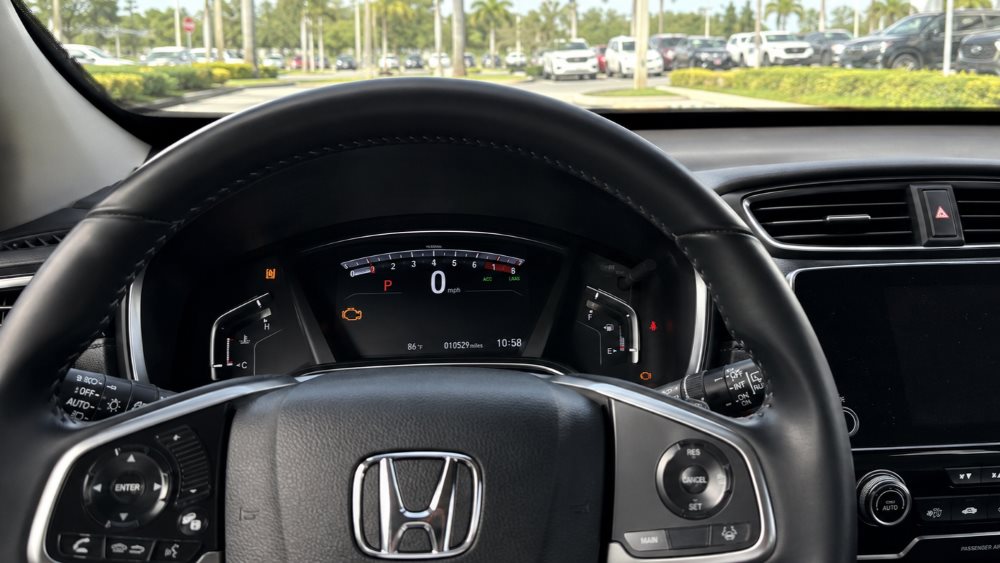 Honda CR-V dashboard with the amber check engine light illuminated in Miami daylight