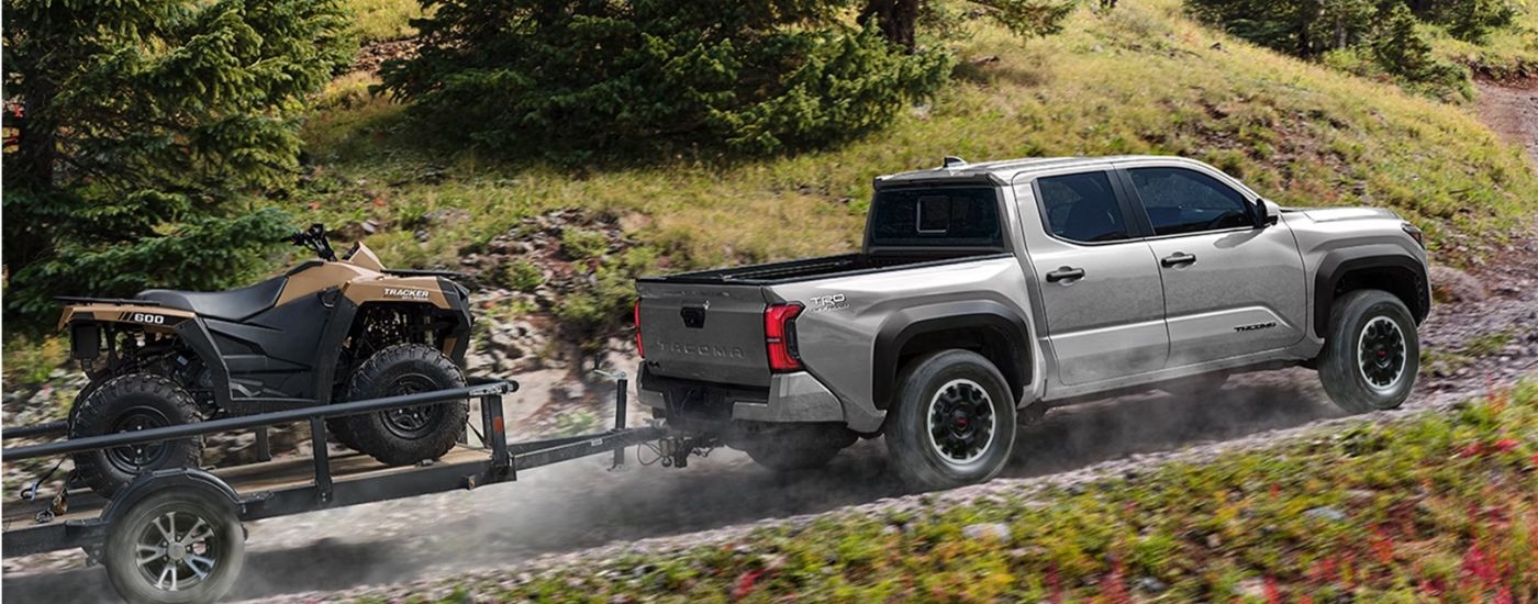 Grey 2026 Toyota Tacoma towing an ATV on a trailer.