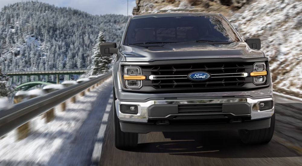 A gray 2026 Ford F-150 Lariat driving on a snow-lined road.
