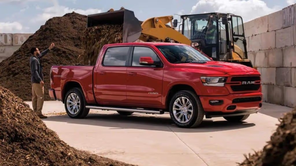 2021 red dodge ram 1500 in a construction site with soil being dumped into the truck bed by a construction vehicle