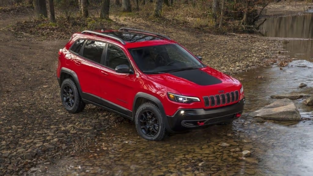 red 2021 jeep cherokee vehicle in the woods making its approach to drive through a shallow rocky river 