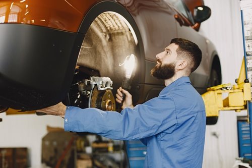 Mechanic working on car disc brake, inspecting for wear and maintenance
