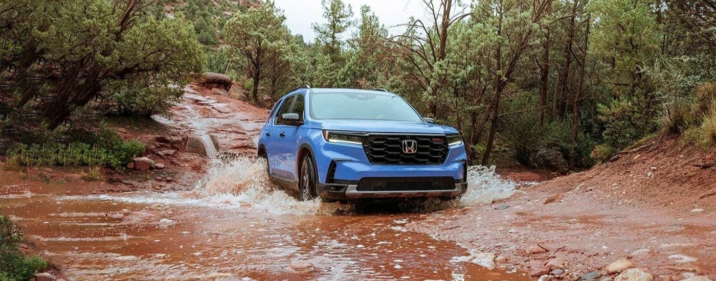 A blue 2023 Honda Pilot TrailSport driving through mud.