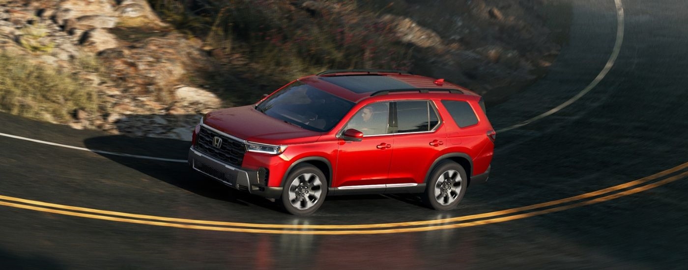 A red 2026 Honda Pilot shown driving a curvy paved road.