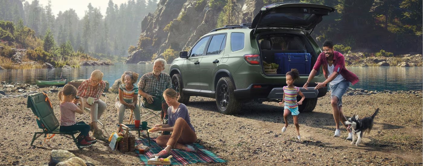 Green 2026 Honda Pilot parked in front of a lake with a family.