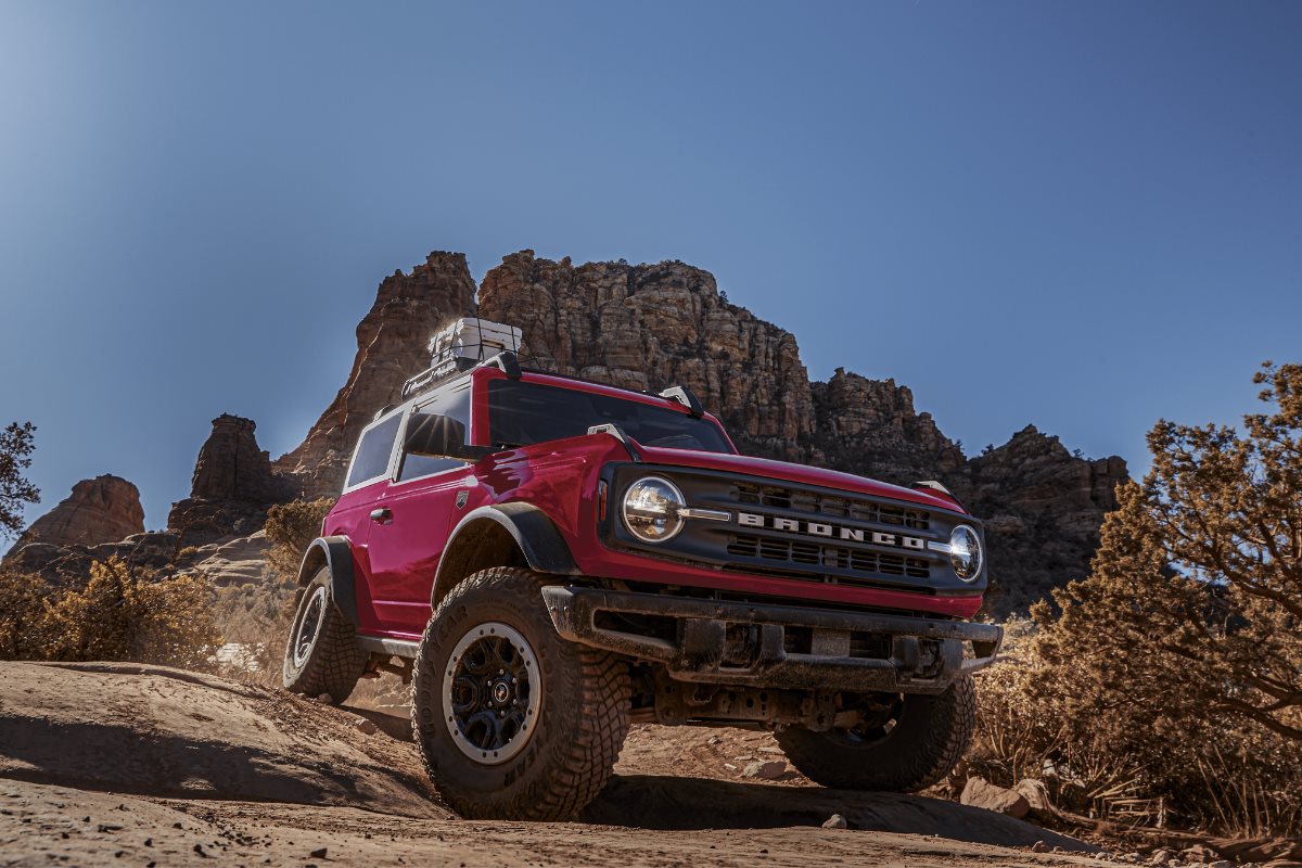 Red Ford Bronco driving over rocky off-road terrain, showcasing its rugged design and trail-ready capability