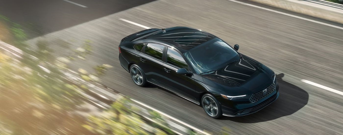 Black 2026 Honda Accord aerial view driving on a paved road.