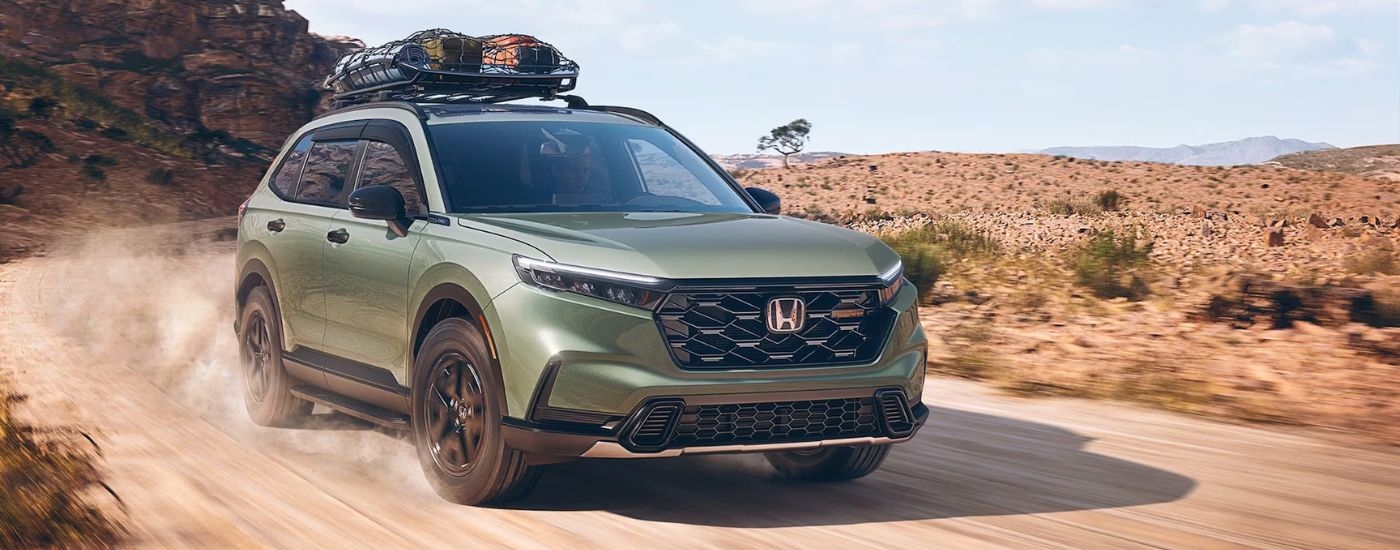 Green 2026 Honda CR-V TrailSport with camping gear on the roof driving off-road.