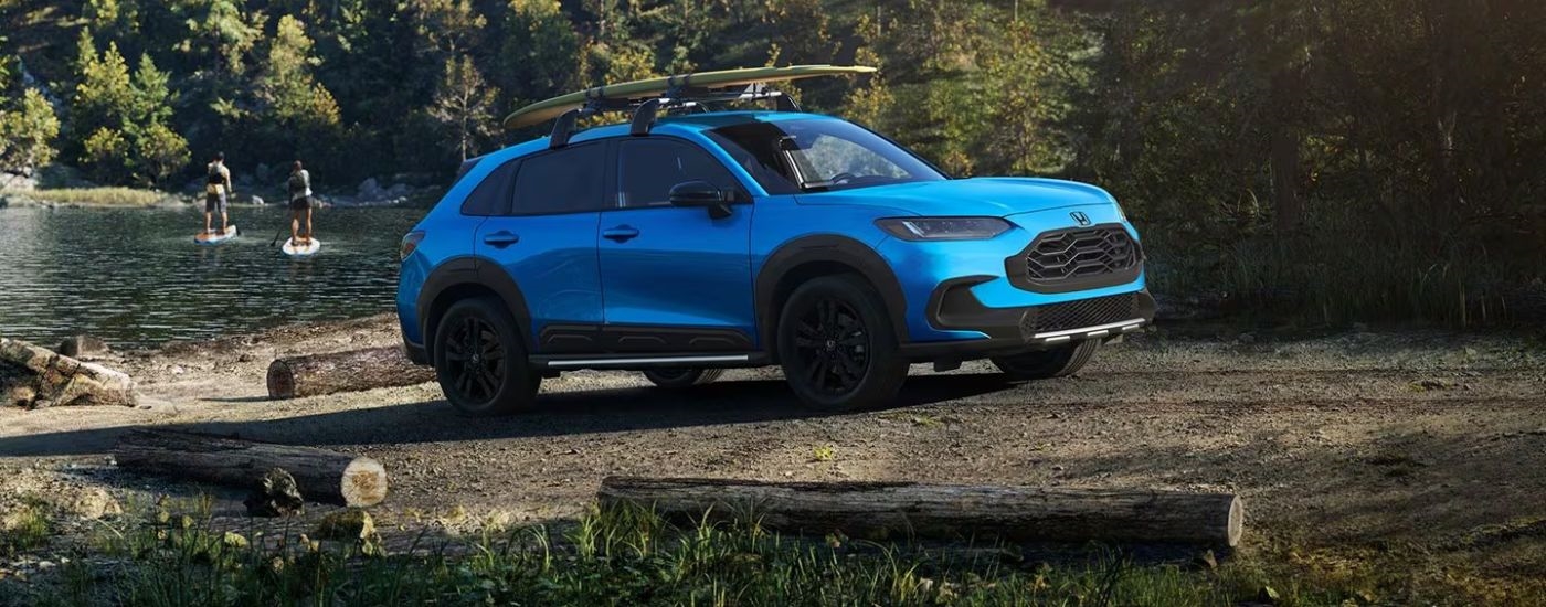 Blue 2027 Honda HR-V Sport with paddleboards on the roof parked near a lake.