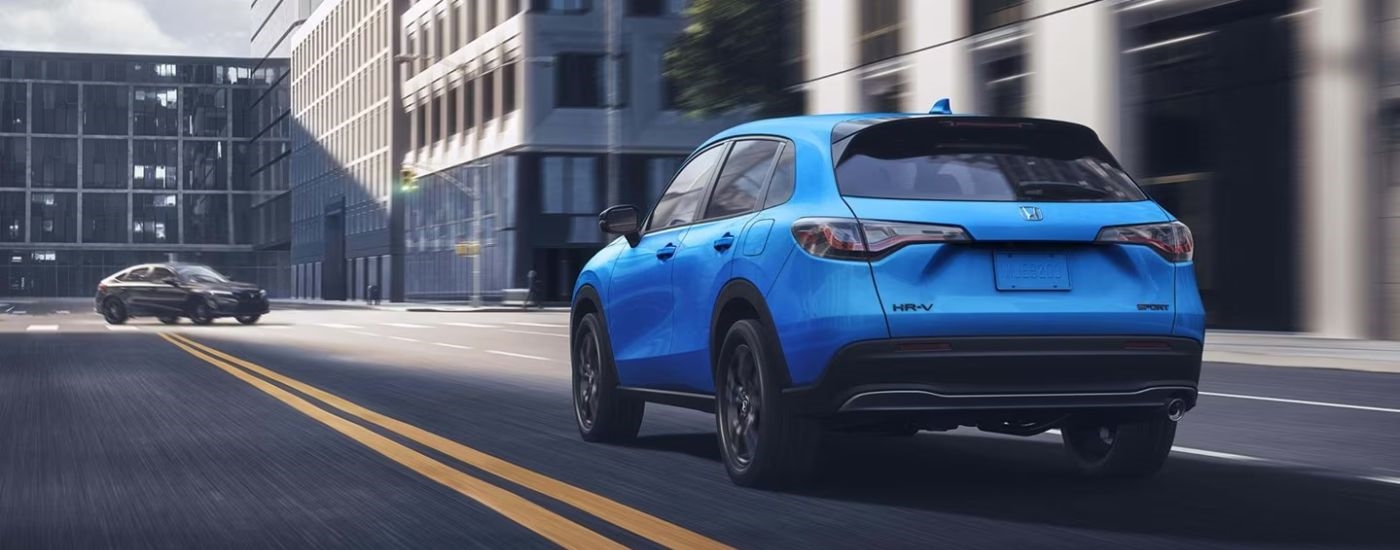 Rear view of a blue 2027 Honda HR-V Sport driving on a paved road.