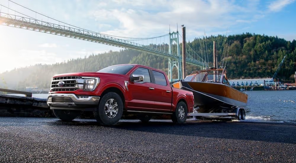 A red 2022 Ford F-150 Lariat is shown towing a boat out of a lake.