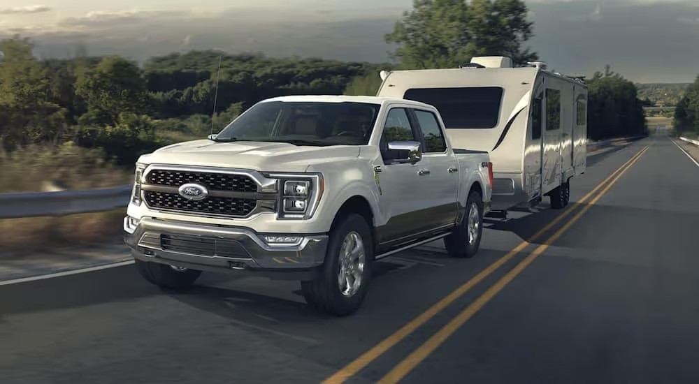 A white 2023 Ford F-150 towing a trailer on an open road.
