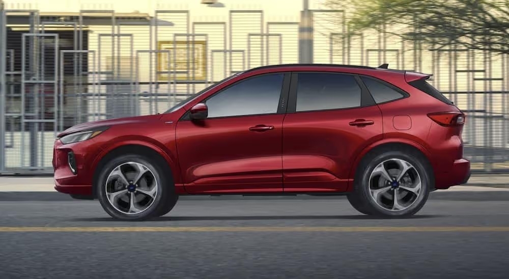 Side view of a red 2023 Ford Escape driving through a city.