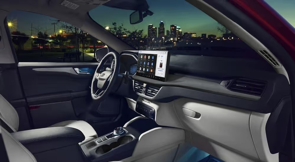 The black and grey interior of a 2023 Ford Escape with infotainment screen and nighttime cityscape outside
