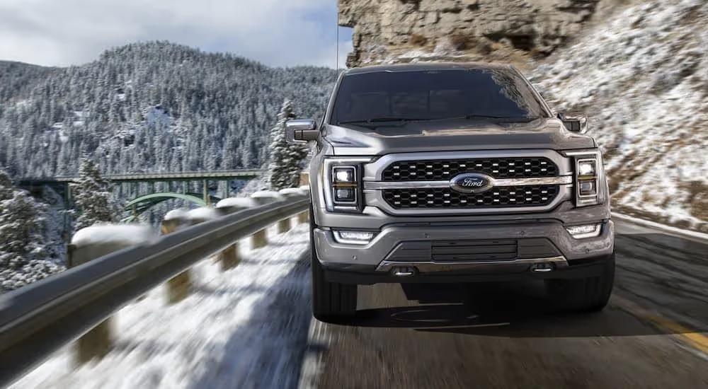 A grey 2021 Ford F-150 driving on a snowy mountain road