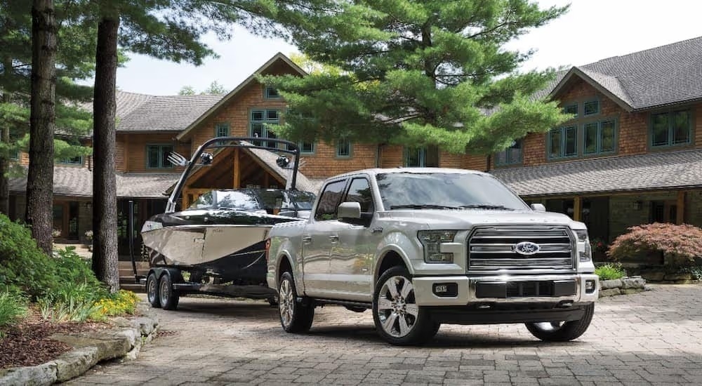 A white 2016 Ford F-150 Limited towing a boat in front of a large rustic home