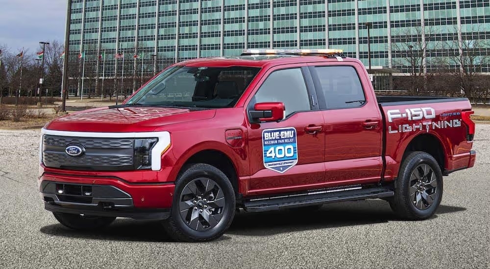 A red 2022 Ford F-150 Lightning pace car in front of the Ford headquarters.