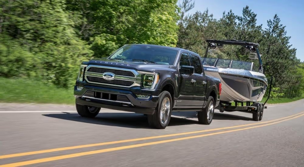 A black 2021 Ford F-150 Hybrid towing a boat on a tree-lined highway