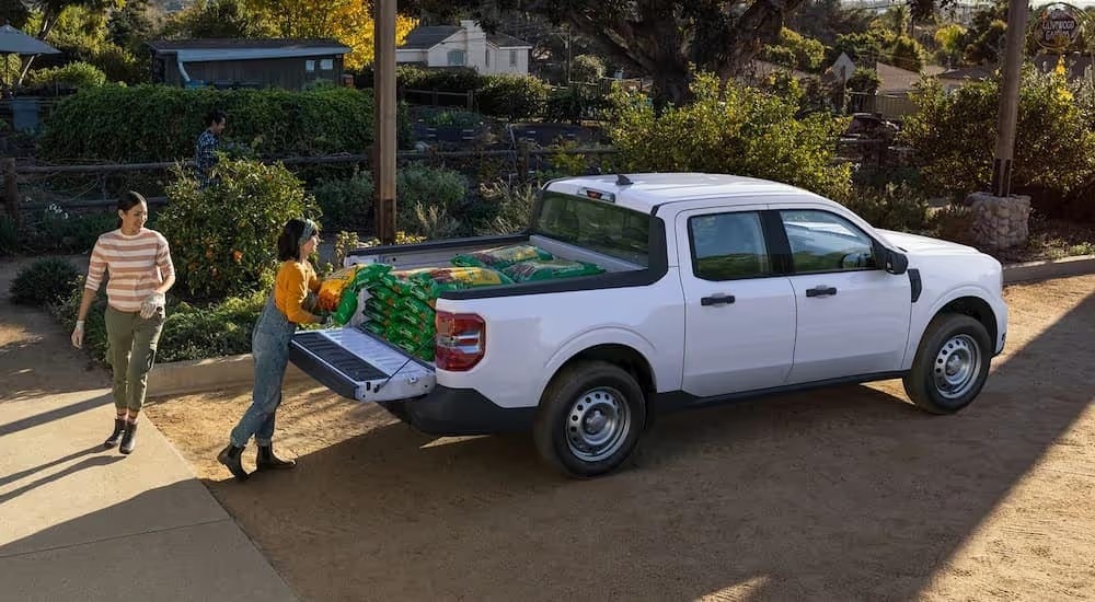 Two women loading soil into the bed of a white 2022 Ford Maverick parked near a garden