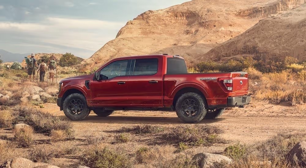 Hikers walking near a red 2023 Ford F-150 Rattler parked in a mountainous desert
