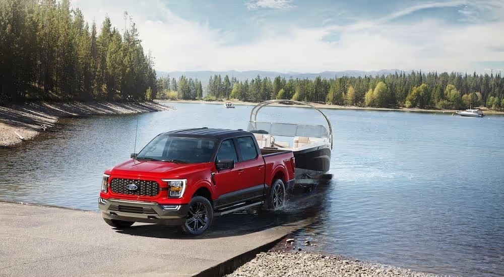A red 2023 Ford F-150 towing a boat out of a lake in the woods