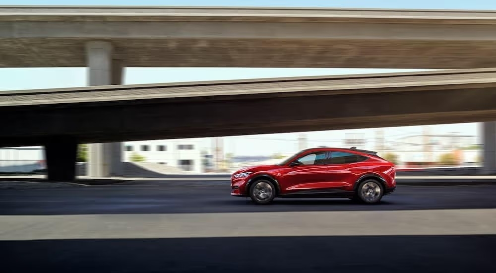 A red 2022 Ford Mustang Mach-E Premium driving by concrete overpasses