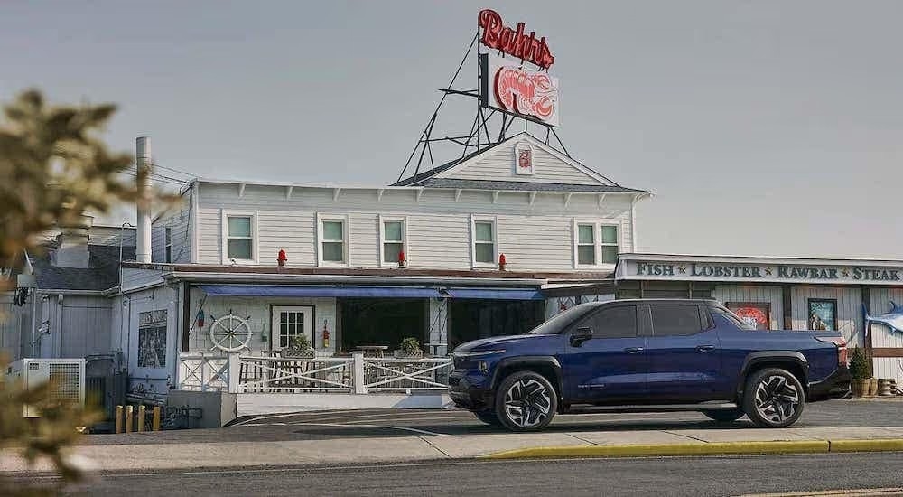 A blue 2024 Chevy Silverado EV parked outside a coastal seafood restaurant. 