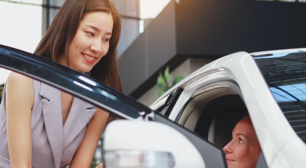 A salesperson is shown helping a customer look at a certified pre-owned vehicle.