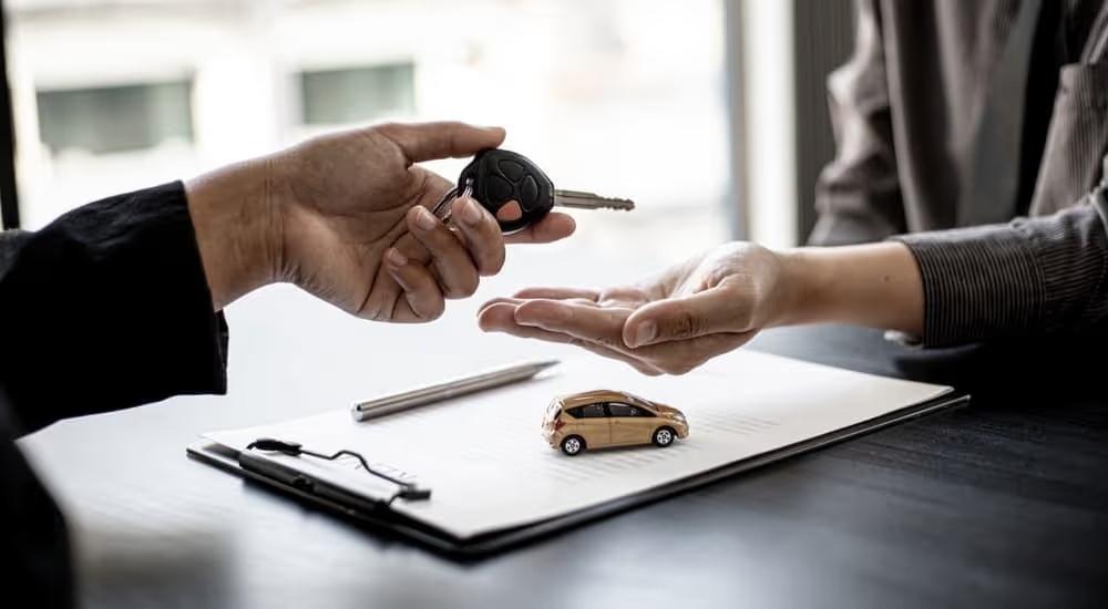 A customer is shown handing a car key to a salesman at a dealership.