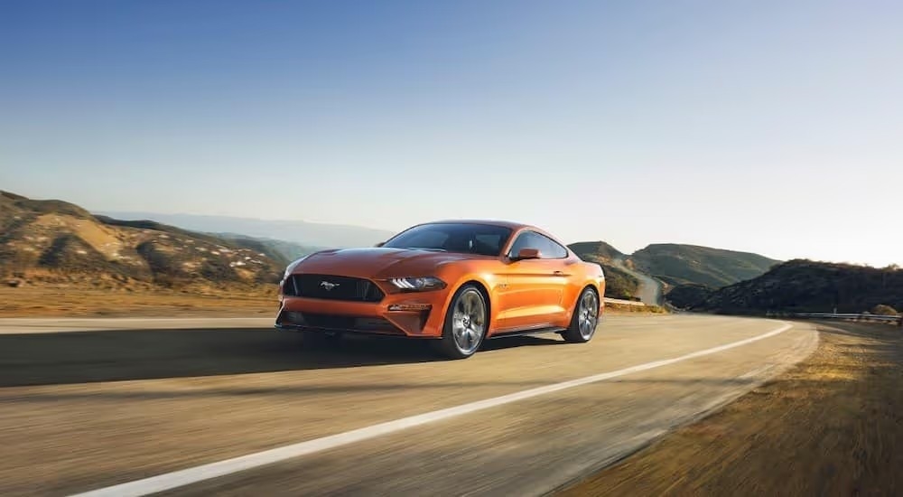 An orange 2018 Ford Mustang is shown driving on an empty highway.