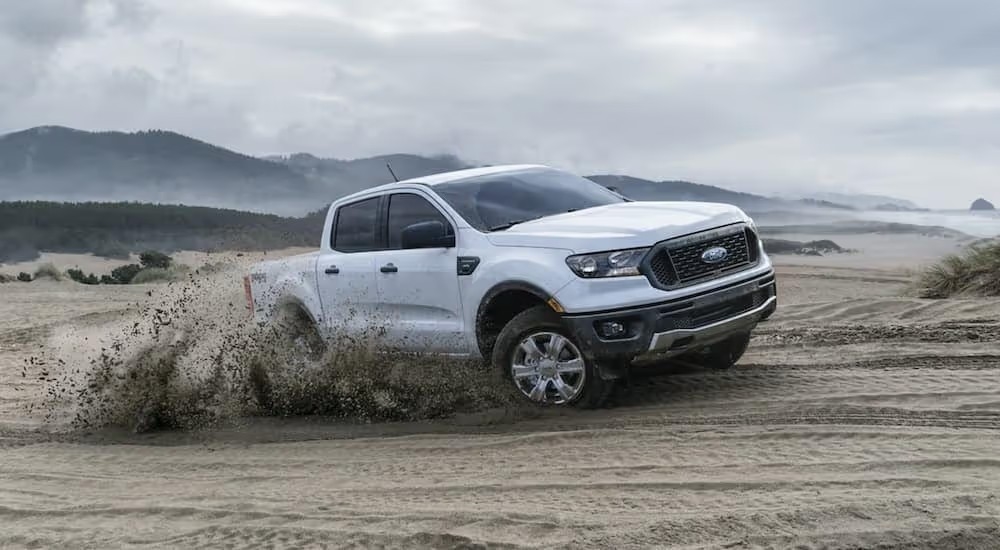 A white 2019 Ford Ranger is shown off-roading on a sandy beach.