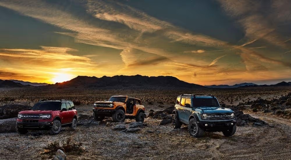A red, an orange, and a blue 2021 Ford Bronco are shown parked in a desert area after leaving a Tennessee Ford Bronco dealer.