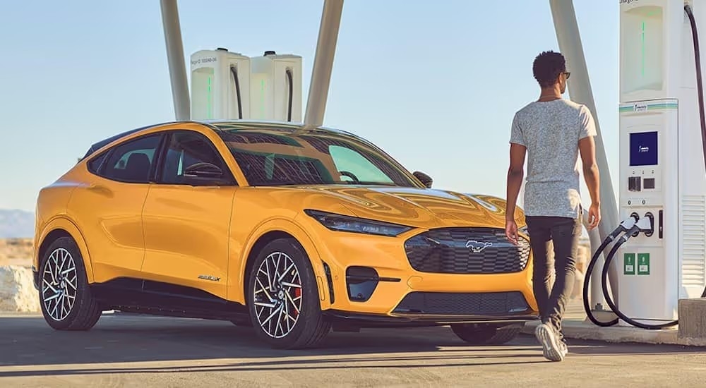 A yellow 2021 Ford Mustang Mach-E is shown parked next to a charging station.