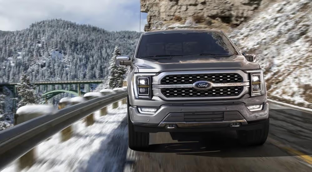 A silver 2021 Ford F-150 Hybrid is driving along a mountain road.