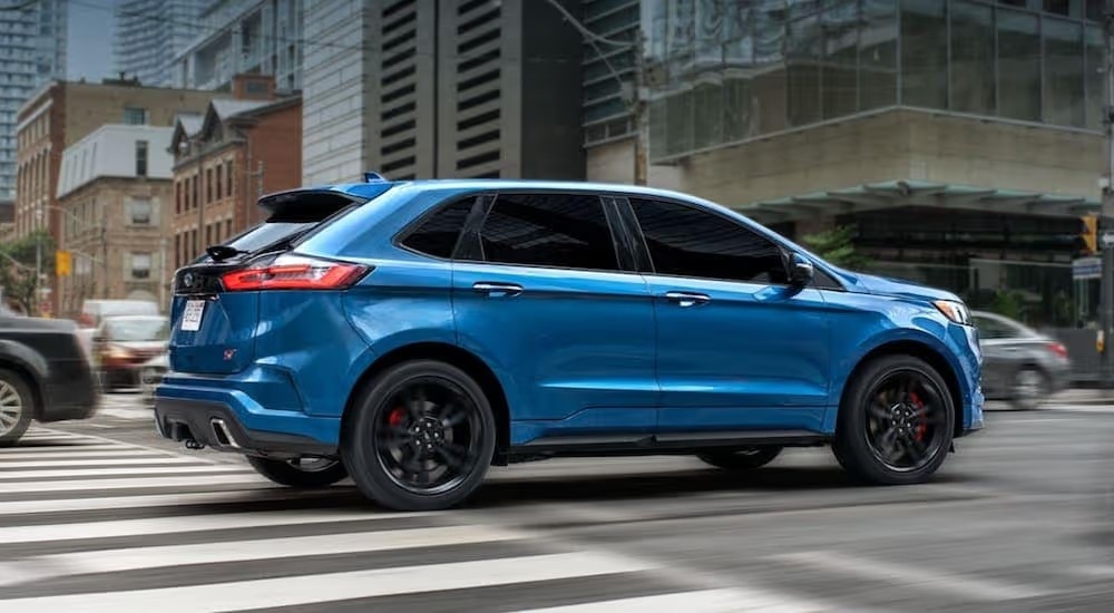 A blue 2021 Ford Edge ST is driving on a city street.