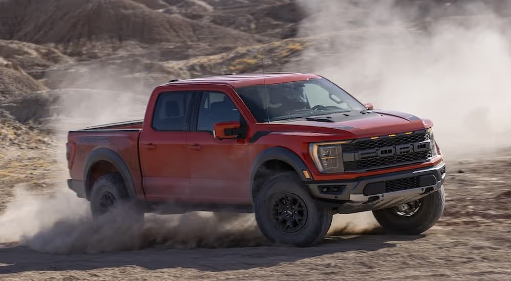 A red 2023 Ford F-150 Raptor kicks up dust while off-roading.