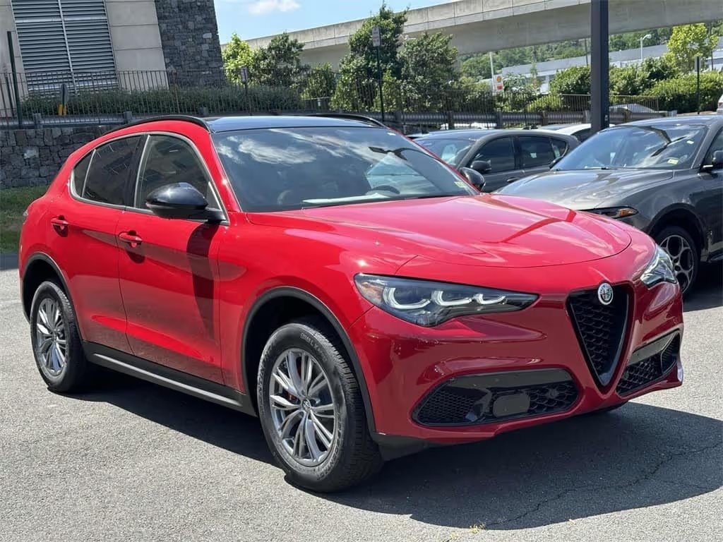 A red 2024 Alfa Romeo Stelvio Sprint SUV parked in a spacious parking lot, showcasing its sleek design and vibrant color.