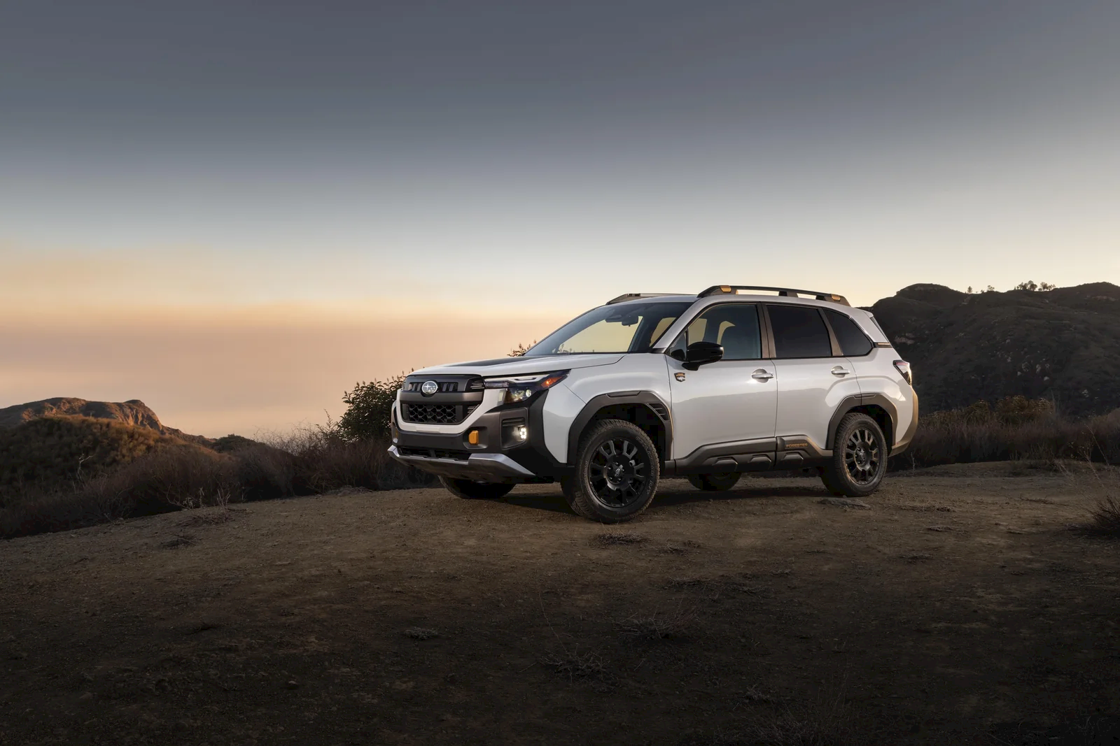 2026 Subaru Forester Wilderness in white parked on a high desert ridge at dusk, showing the copper accents, black wheel-arch cladding, all-terrain tires, and roof rails.