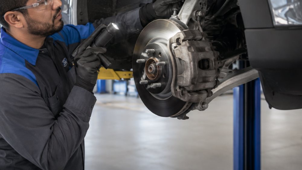 Worn Ford brake pad and rotor next to new Motorcraft replacement parts in a Chicago service bay