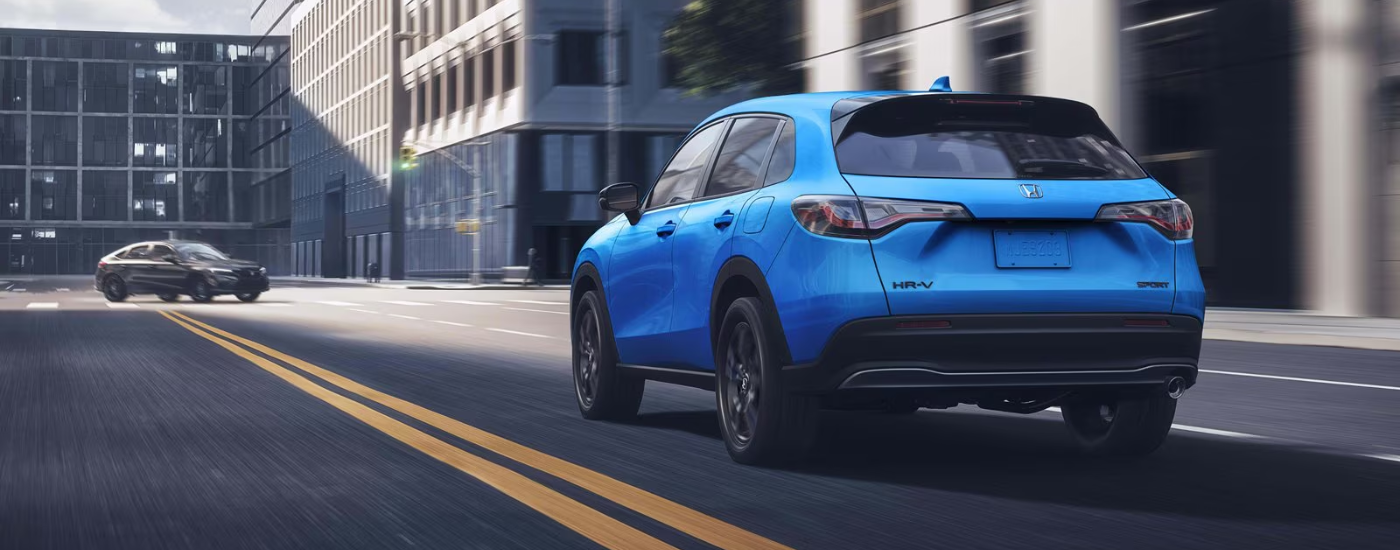 Rear of a blue 2027 HR-V Sport driving down a road.