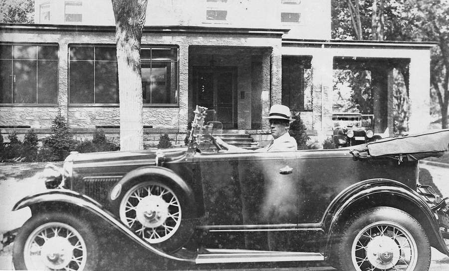 Harry Dahl at the wheel of an open touring car outside a house