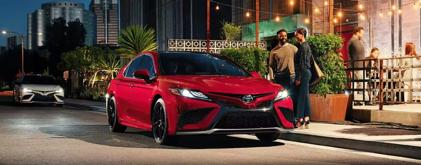 Red 2023 Toyota Camry parked on the side of the road with a couple nearby.