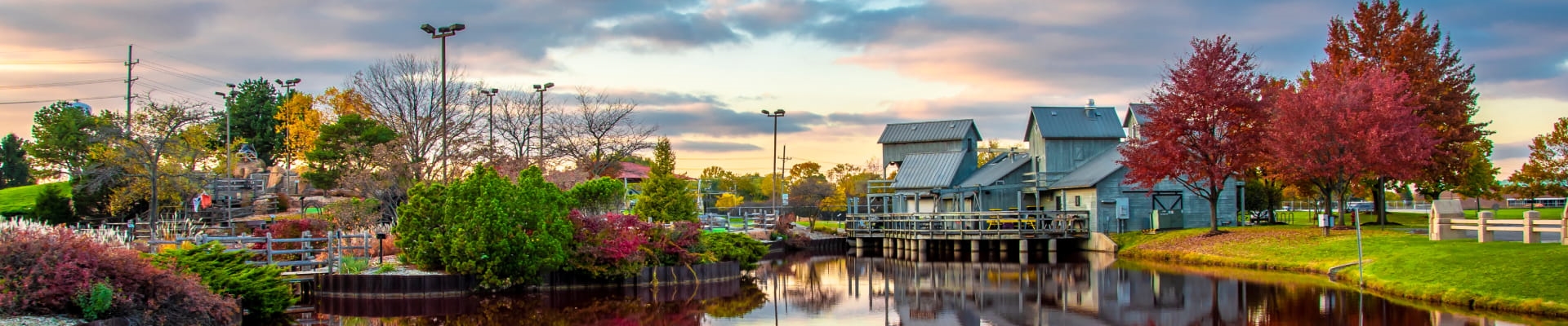 Scenic park with autumn trees, rustic buildings, and a pond reflecting the colorful landscape.