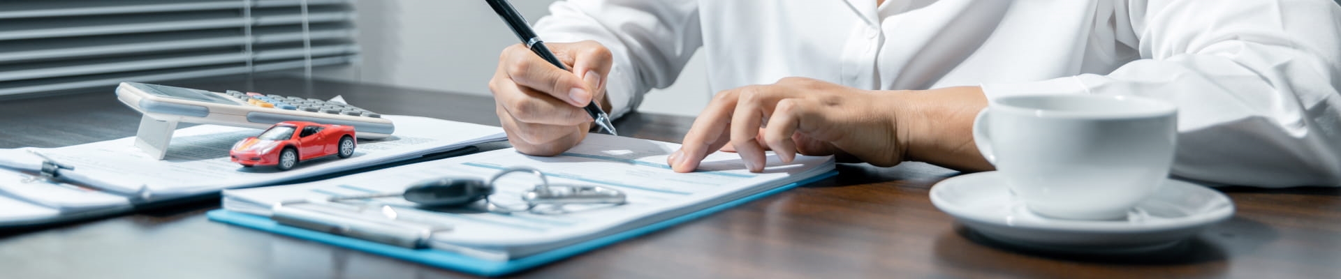 Person reviewing and signing automotive finance documents at a desk with a calculator and small model car.