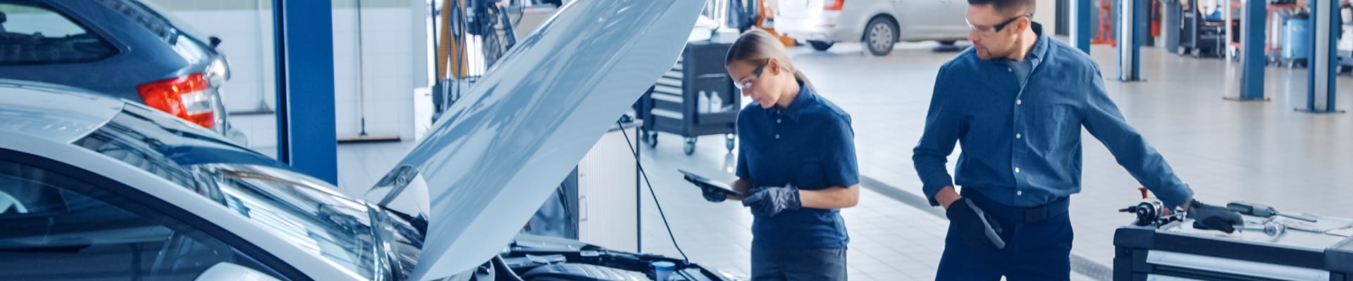 Two automotive technicians inspecting a vehicle with its hood open inside a service center.