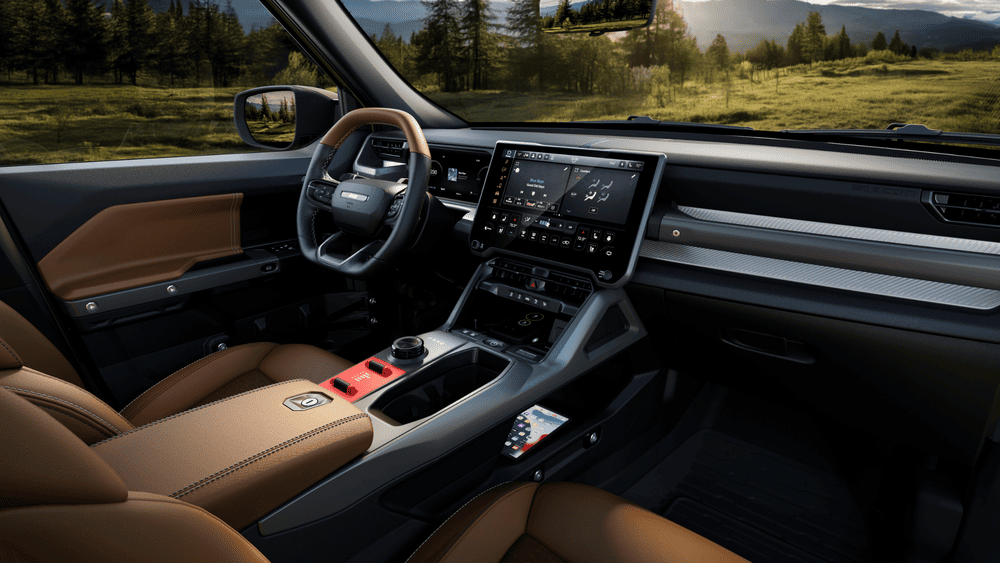 2026 Jeep Recon interior in Margate FL featuring tan leather seats, wide touchscreen infotainment display, red off-road toggle switches on center console, and carbon fiber trim accents