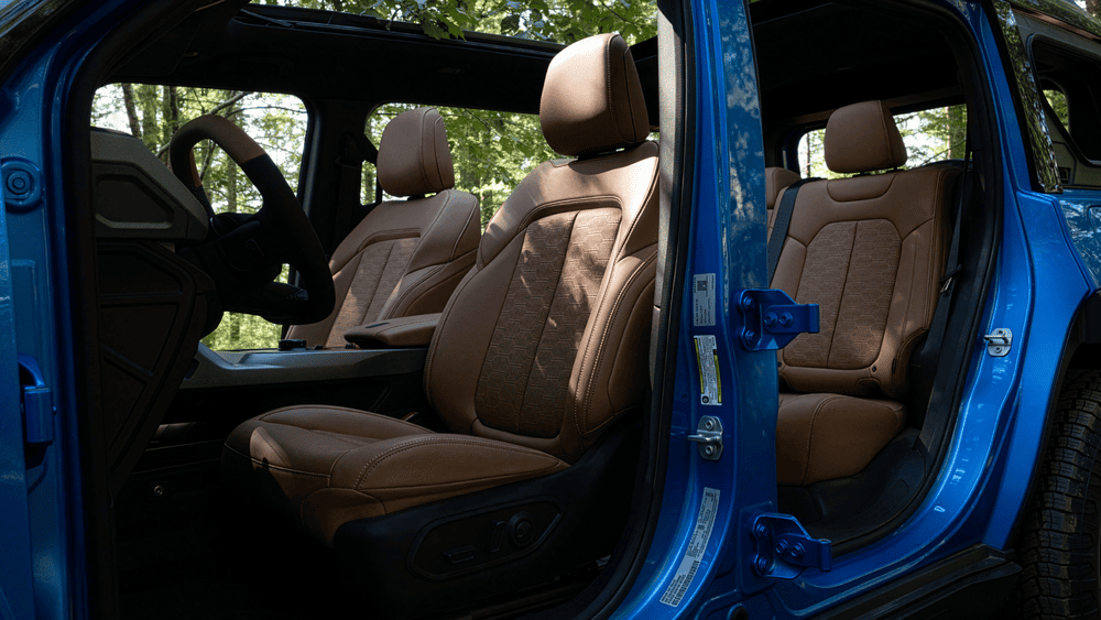 2026 Jeep Recon interior in Margate FL with doors-off view showing tan leather front and rear seats with textured fabric inserts and blue door frame accent hardware